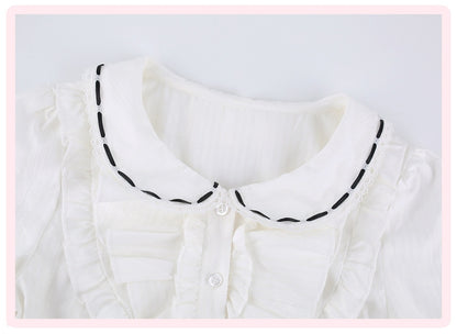 White ruffled blouse with a Peter Pan collar featuring black dashed contrast stitching, shown in a close-up shot.
