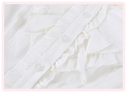 Close-up detail of a white ruffled blouse or dress, showing layered ruffles and decorative buttons on a light pink border background.