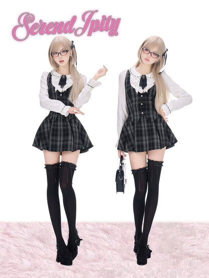Two models wearing matching Lolita-style outfits from Serendipity, featuring a black and gray plaid pinafore dress over a white long-sleeve blouse, paired with black thigh-high stockings and black shoes, set against a white background with a pink faux fur floor and pink logo text.