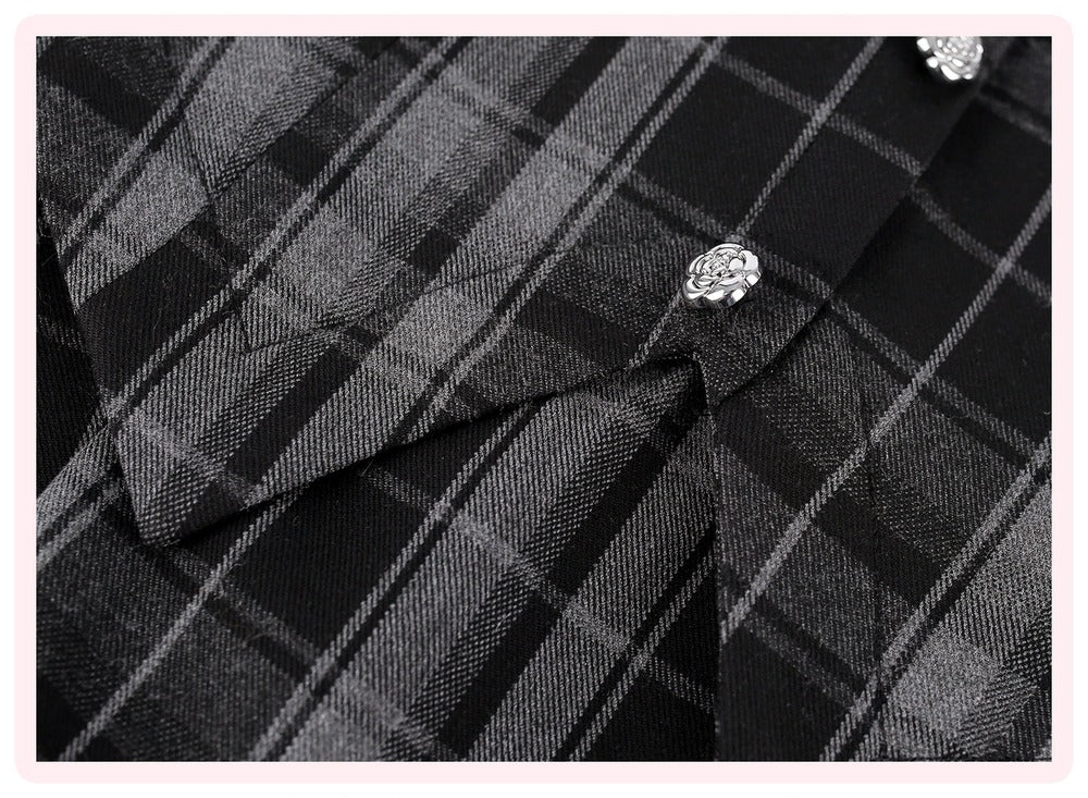 Close-up of a black and gray plaid shirt fabric with decorative silver floral buttons, framed by a light pink border.