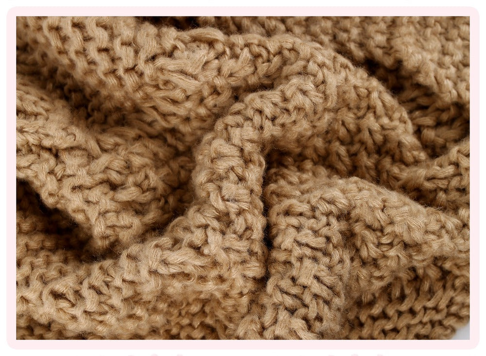 A close-up of a chunky knit blanket in a warm camel brown color, showing the detailed texture of the yarn.