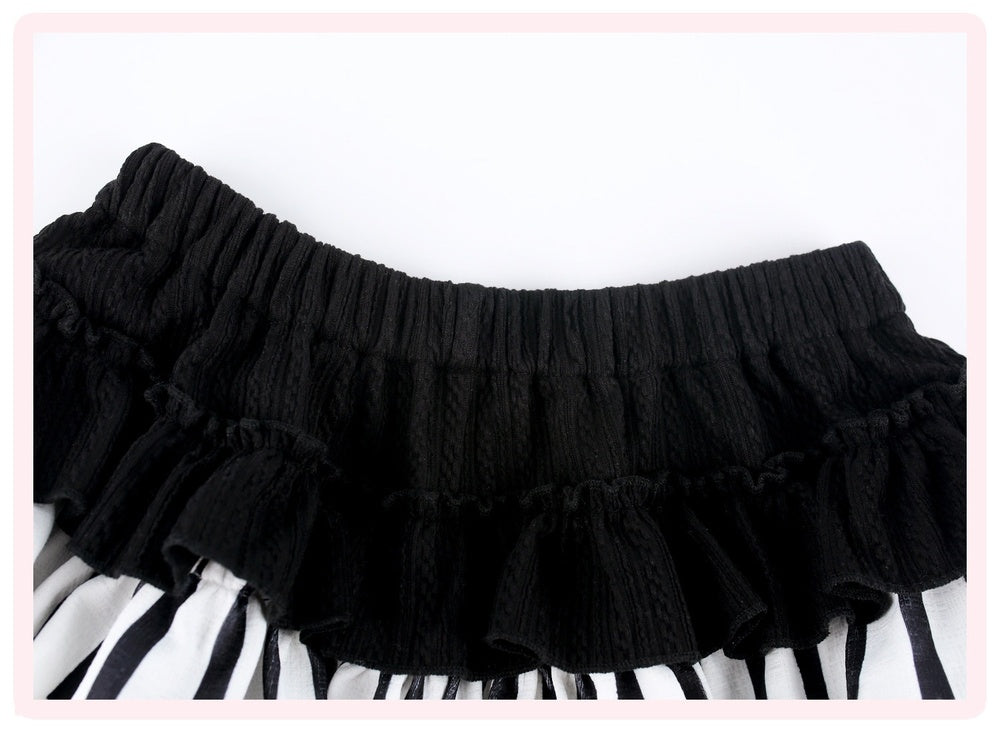 Black pleated ruffled skirt with a textured knit waistband, shown laid flat against a white background with a pink border.