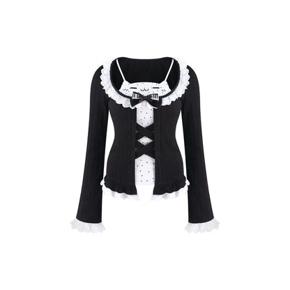 A black long-sleeve ribbed top with white ruffled trim, a white polka-dot front panel, and a black bow at the neckline, shown on a plain white background.