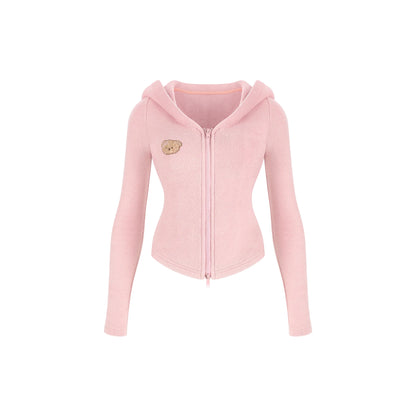 A light pink zip-up hoodie with long sleeves, a hood, and a small embroidered teddy bear face patch on the left chest, shown against a plain white background.