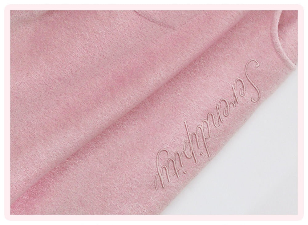 A close-up of a soft pink plush fabric with the word 'Serendipity' embroidered in cursive across a fold, set against a white background with a thin pink border.