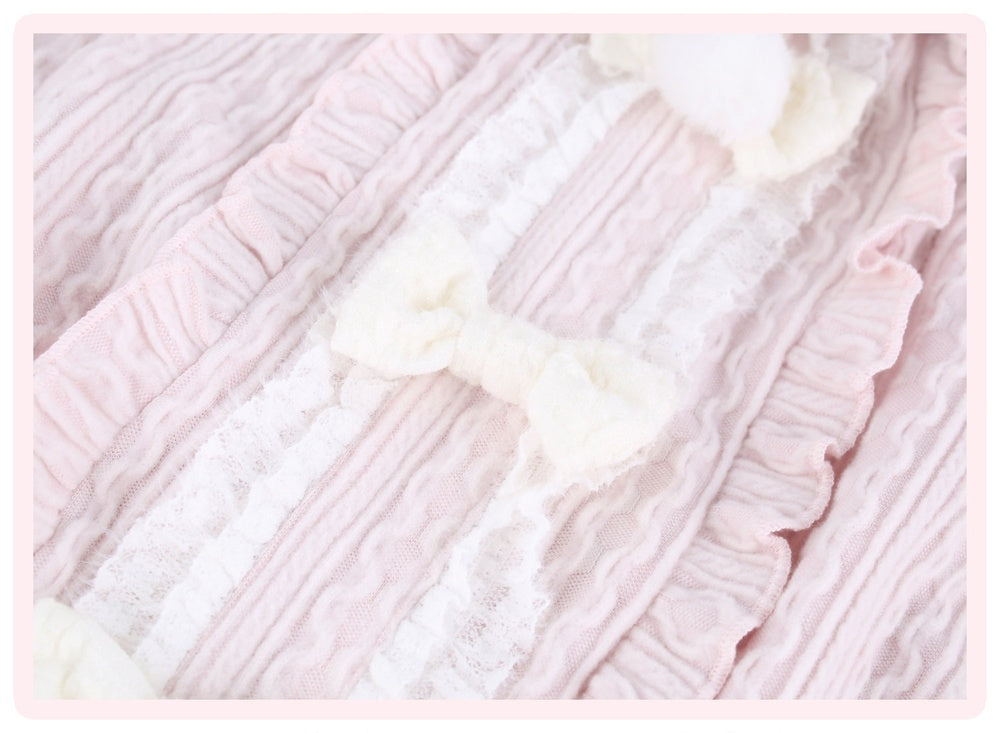 Close-up of a light pink and white ruffled textile with lace trim and soft white bow details, shown as a fabric or garment detail shot.