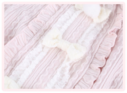 Close-up of a light pink and white ruffled textile with lace trim and soft white bow details, shown as a fabric or garment detail shot.