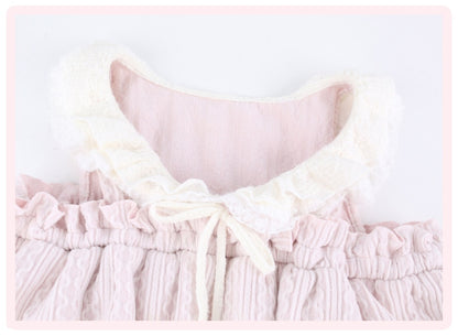A close-up of a babydoll-style dress featuring a soft pink crinkled fabric body with a large cream-colored ruffled collar and a matching cream bow at the center front.