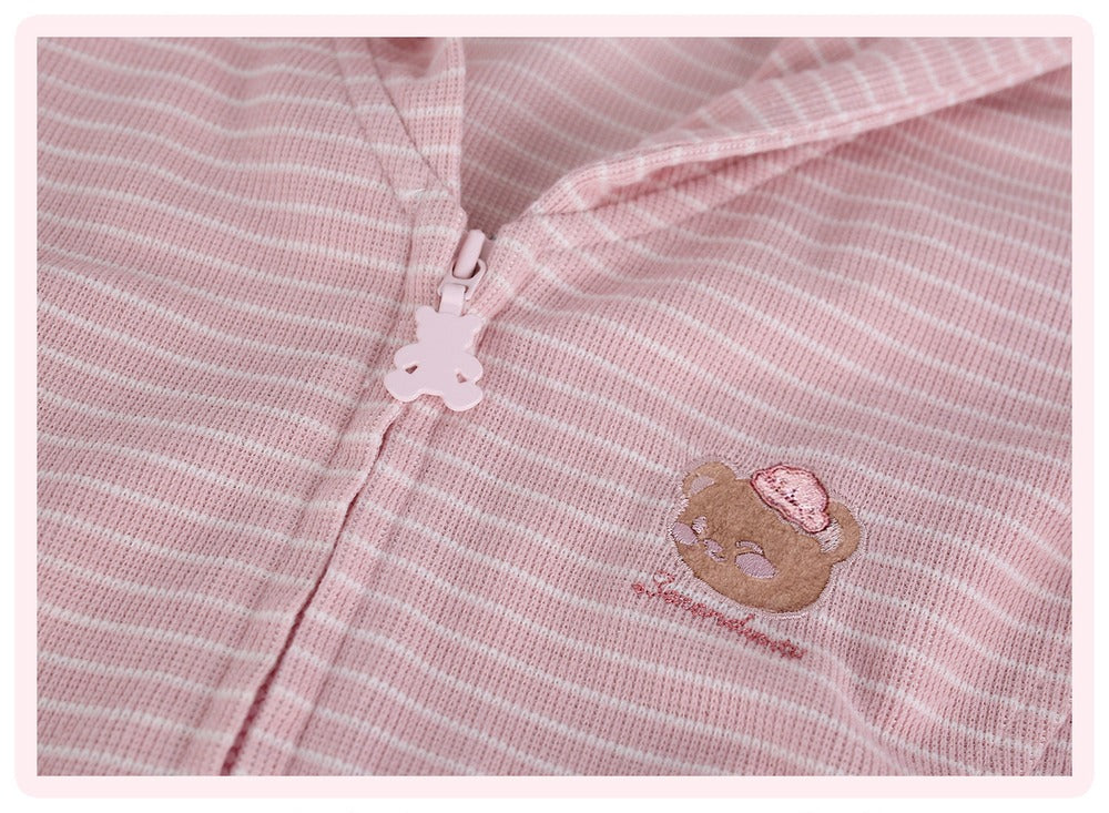 Close-up of a pink and white striped zippered garment, a soft top, featuring a small embroidered teddy bear face with a pink hat on the chest.