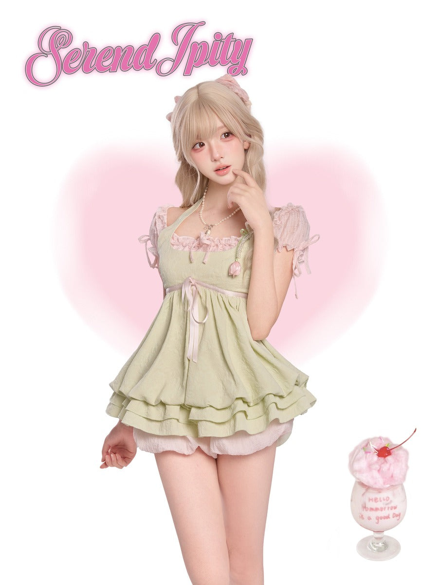 Person wearing a light green dress with ruffles and a cherry on top, standing against a pink background