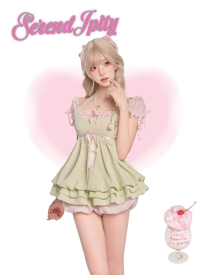 Person wearing a light green dress with ruffles and a cherry on top, standing against a pink background