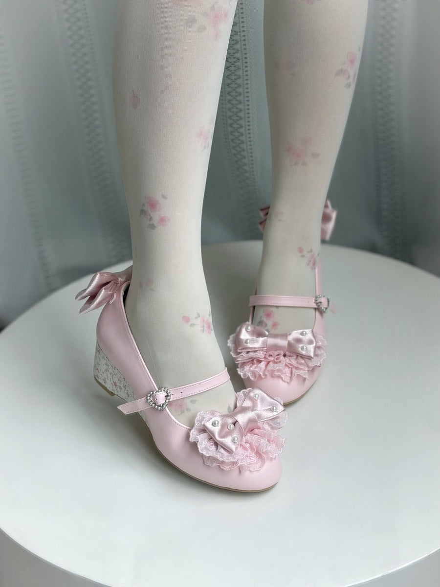 Pink Lolita-style Mary Jane shoes with floral lace and ribbon bows, shown on a model wearing white floral tights, sitting on a white round table.