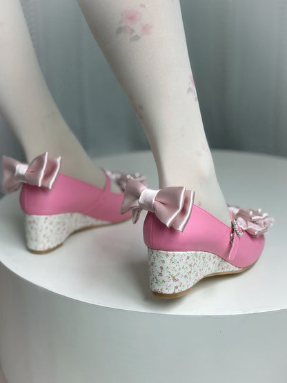 Pink Mary Jane wedge shoes with satin bows and floral wedge heels, shown on a model wearing white tights.