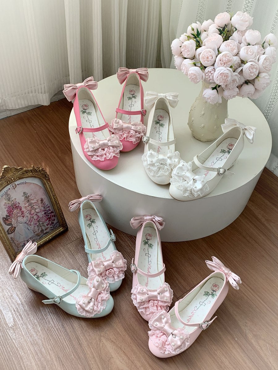 Four decorative Mary Jane-style flats with bows and ruffled floral details are arranged on a round white pedestal and floor. The shoes come in pink, white, mint green, and pale blush tones, with floral prints on the insoles.