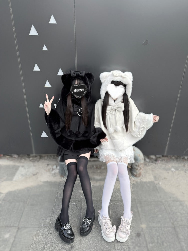 Two people in black and white outfits posing against a gray wall with triangle patterns.