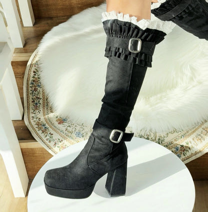 Black knee-high boots with ruffles and buckles on a white platform.