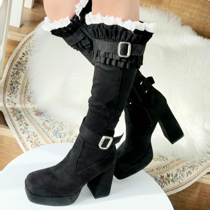 Black knee-high boots with ruffled leg warmers on a white surface.