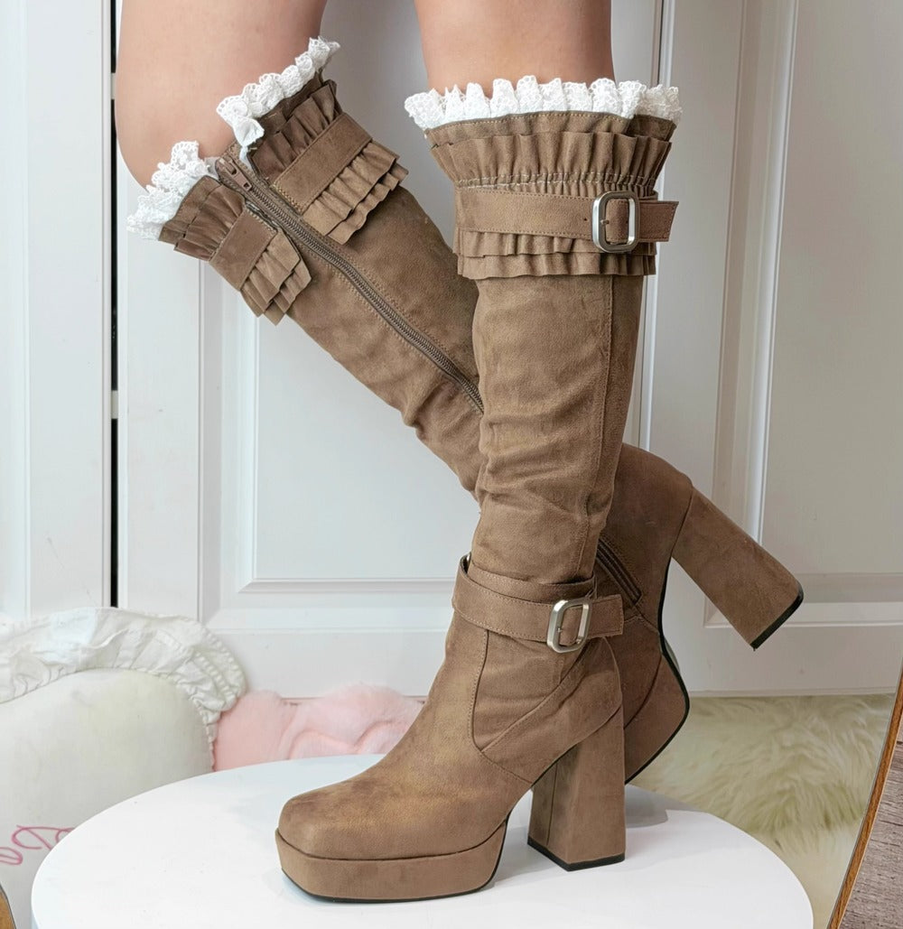 Brown knee-high boots with ruffled details on a white surface.