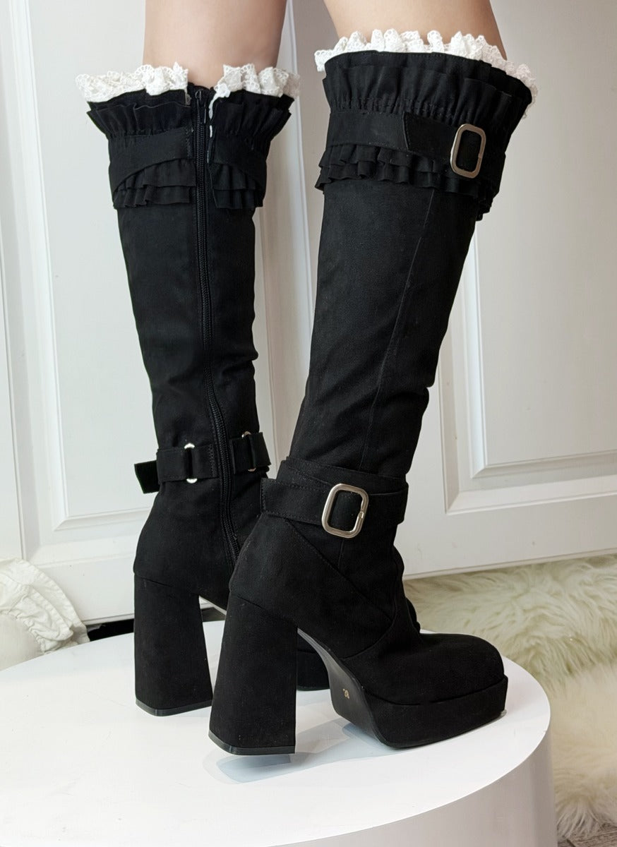 Black knee-high boots with ruffled top and buckles on a white platform.