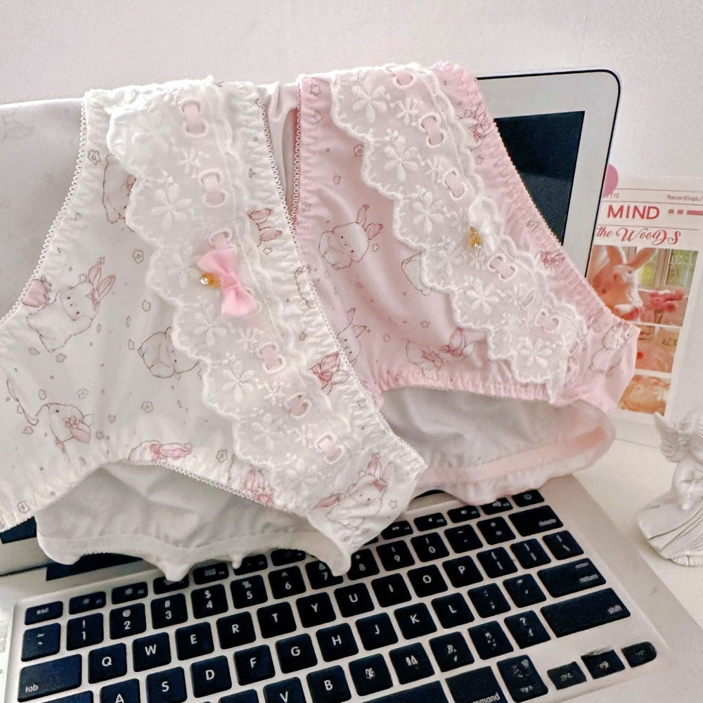 Two pairs of pink and white lace-trimmed panties on a laptop keyboard with a magazine in the background.