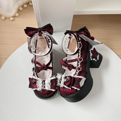 Pair of ornate red and black shoes with bows on a white surface.
