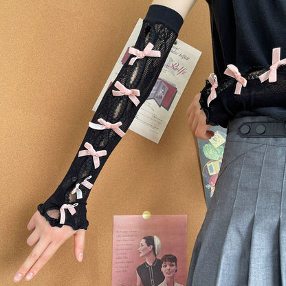 Black lace gloves with pink bows worn by a person on a brown background.