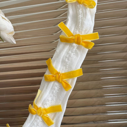 White lace curtain with yellow ribbons against a wooden panel background