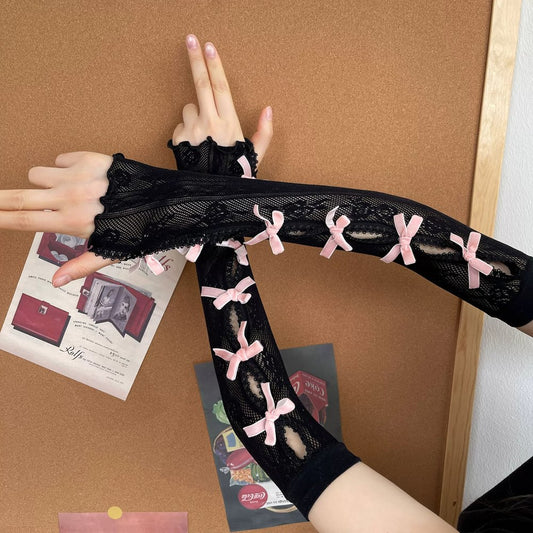 Black lace arm cover with pink bows worn by a person on a corkboard background