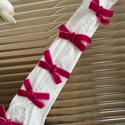 White lace fabric with pink velvet bows against a wooden background