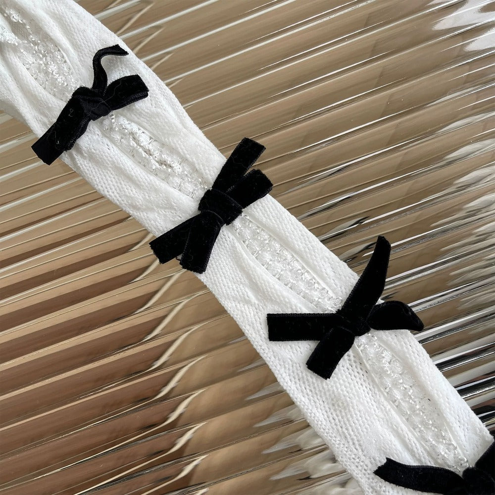 White lace fabric with black velvet bows on a textured beige background