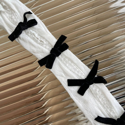 White lace fabric with black velvet bows on a textured beige background