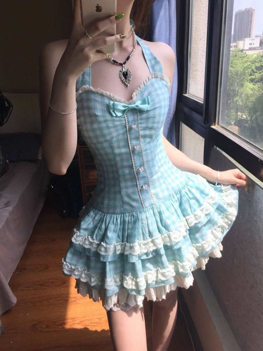 Person wearing a light blue checkered dress with white lace details, standing by a window.