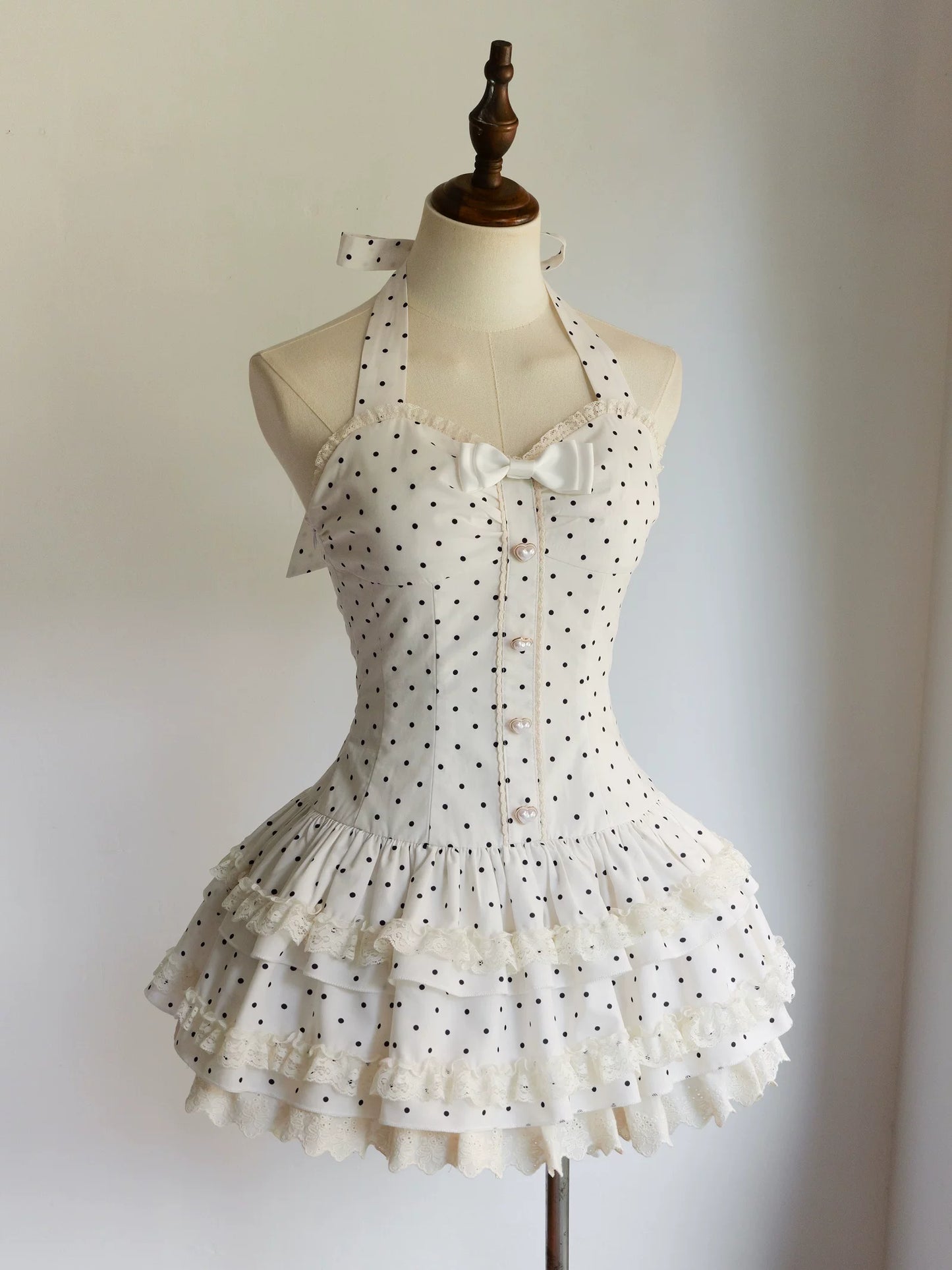 White dress with black polka dots on a mannequin against a plain background