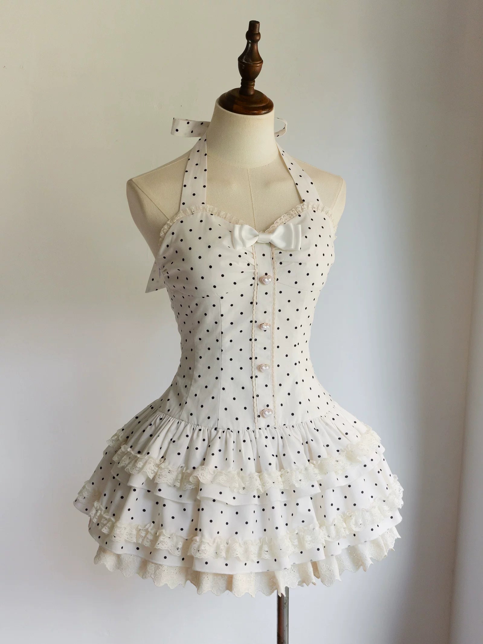 White dress with black polka dots on a mannequin against a plain background