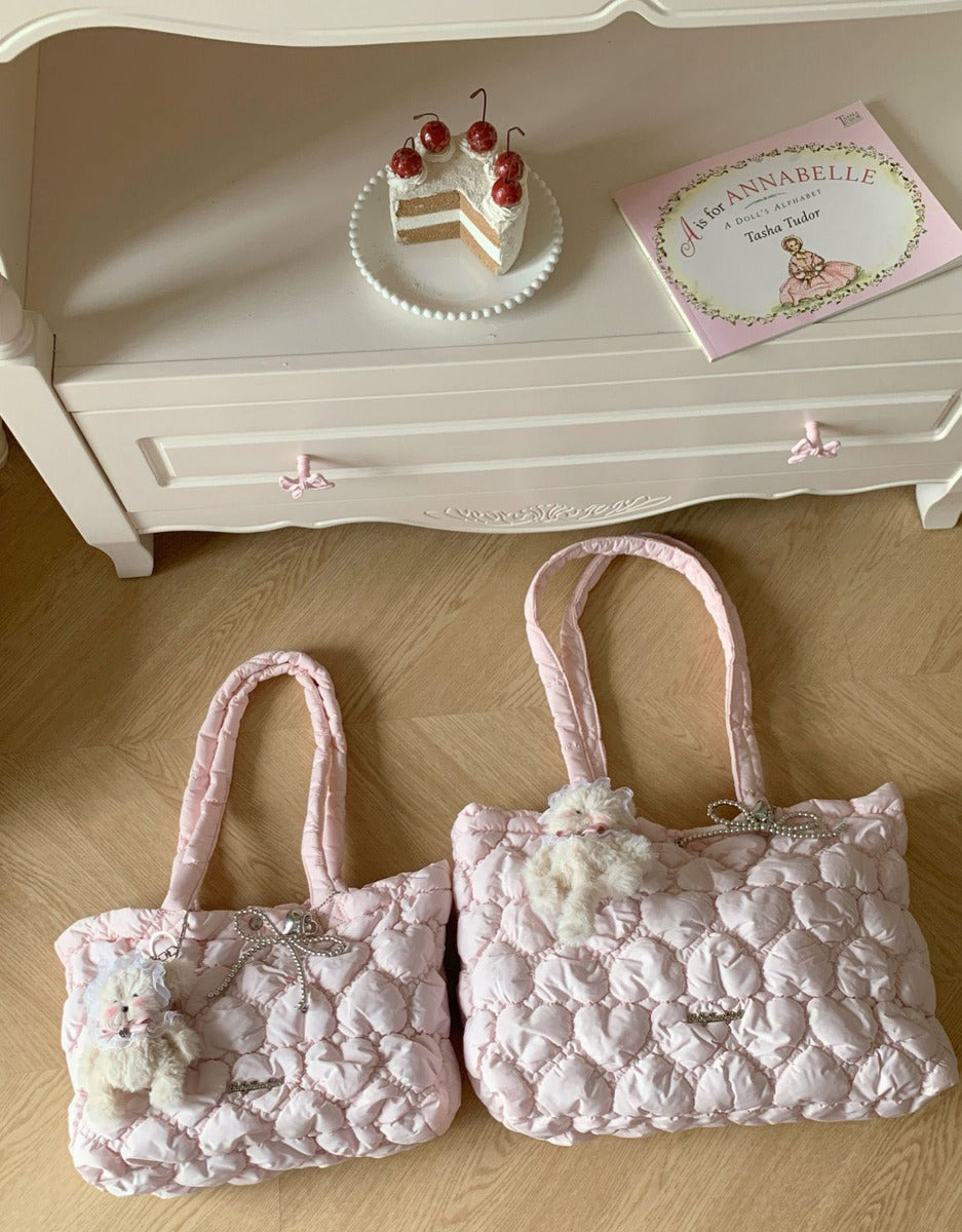 Two light pink quilted shoulder bags with plush white bear charms and bow details, displayed on a wooden floor in front of a white dresser.