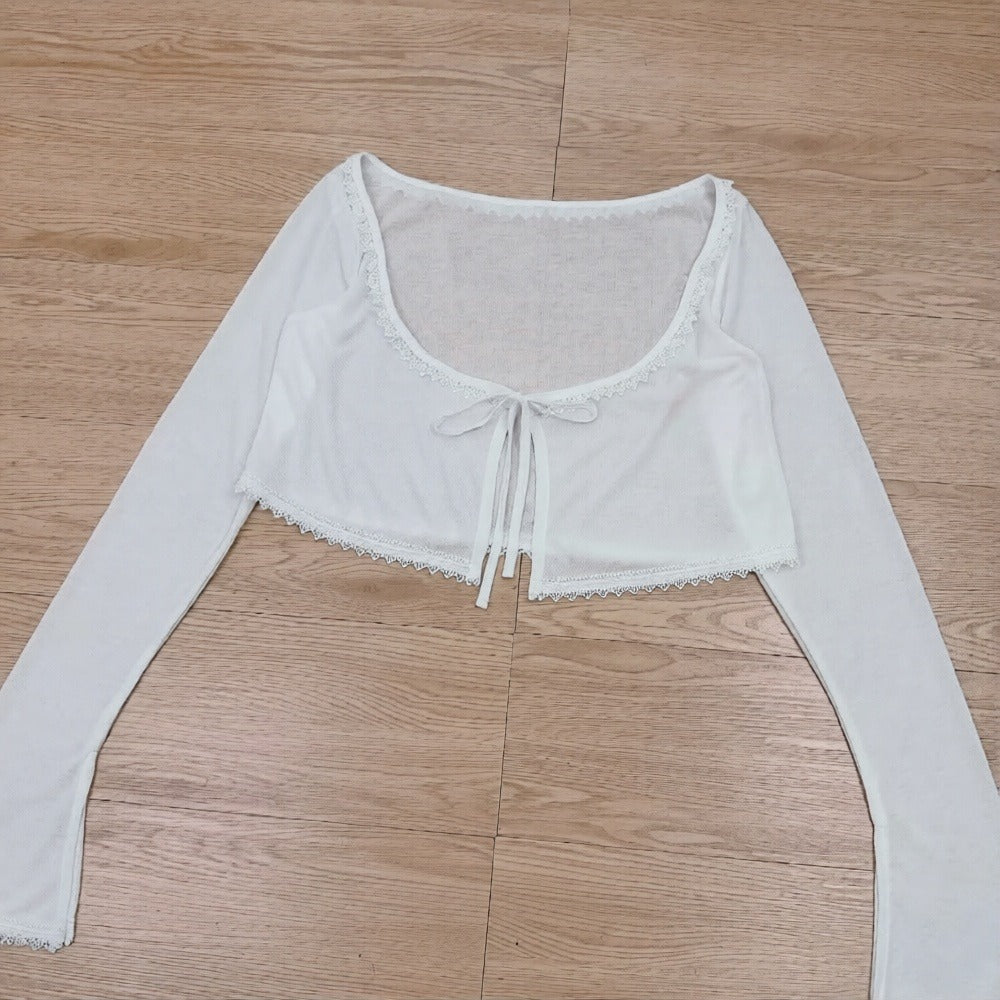 White long-sleeve crop top with lace details on a wooden floor