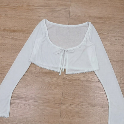 White long-sleeve crop top with lace details on a wooden floor