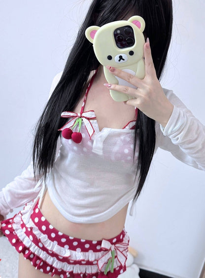 Person wearing a white top with red polka dots and cherry designs, holding a phone case shaped like a bear.
