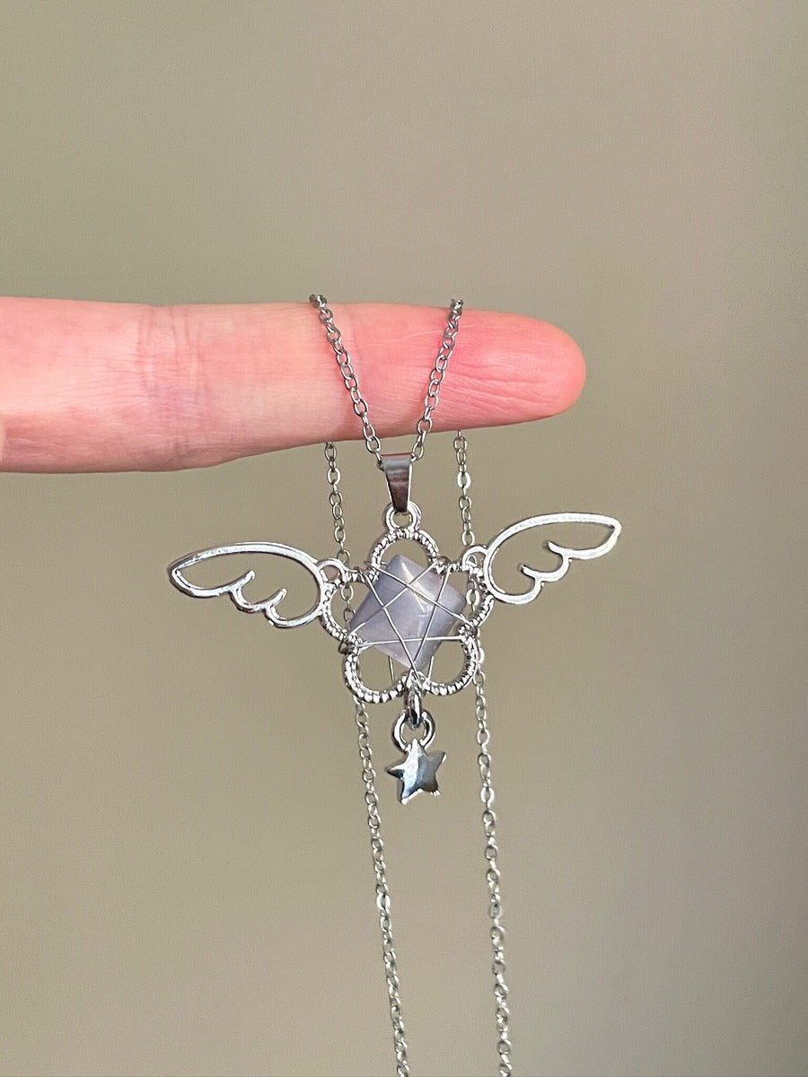 Silver angel wing necklace held by a hand against a beige background