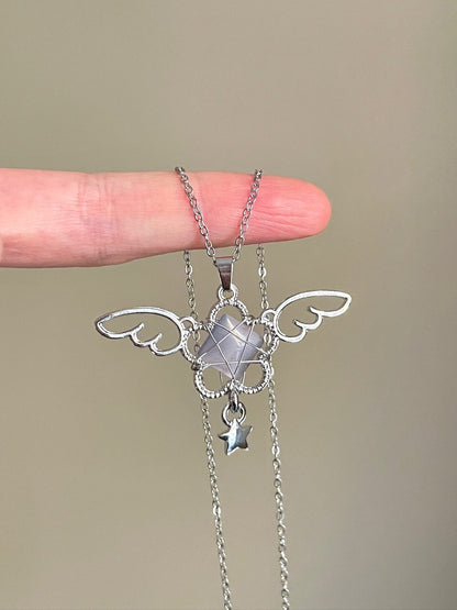 Silver angel wing necklace held by a hand against a beige background