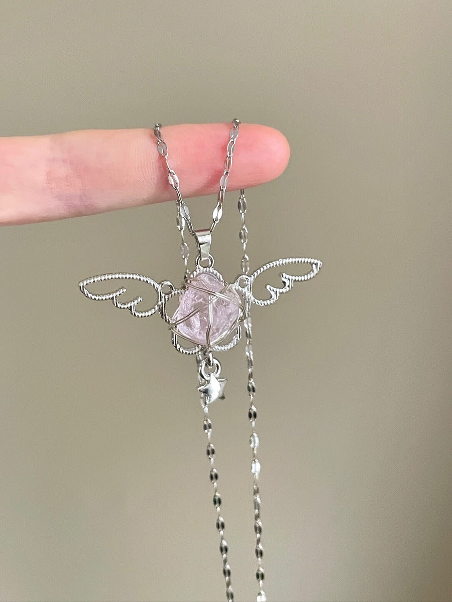 Silver fairy-shaped necklace with a pink stone held between fingers against a neutral background