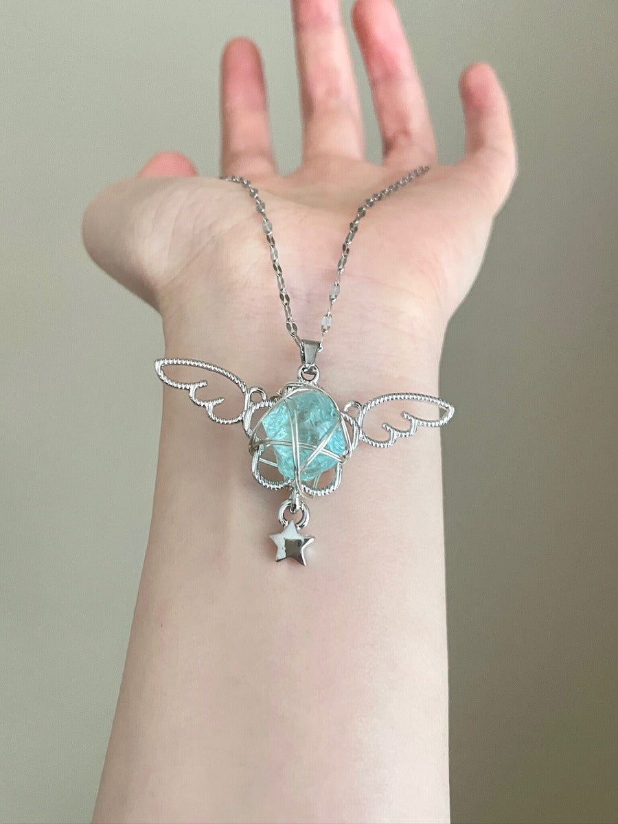 Hand wearing a silver necklace with a green pendant against a neutral background