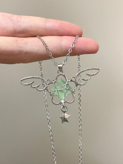 Silver necklace with a green stone and star pendant held by a hand against a neutral background