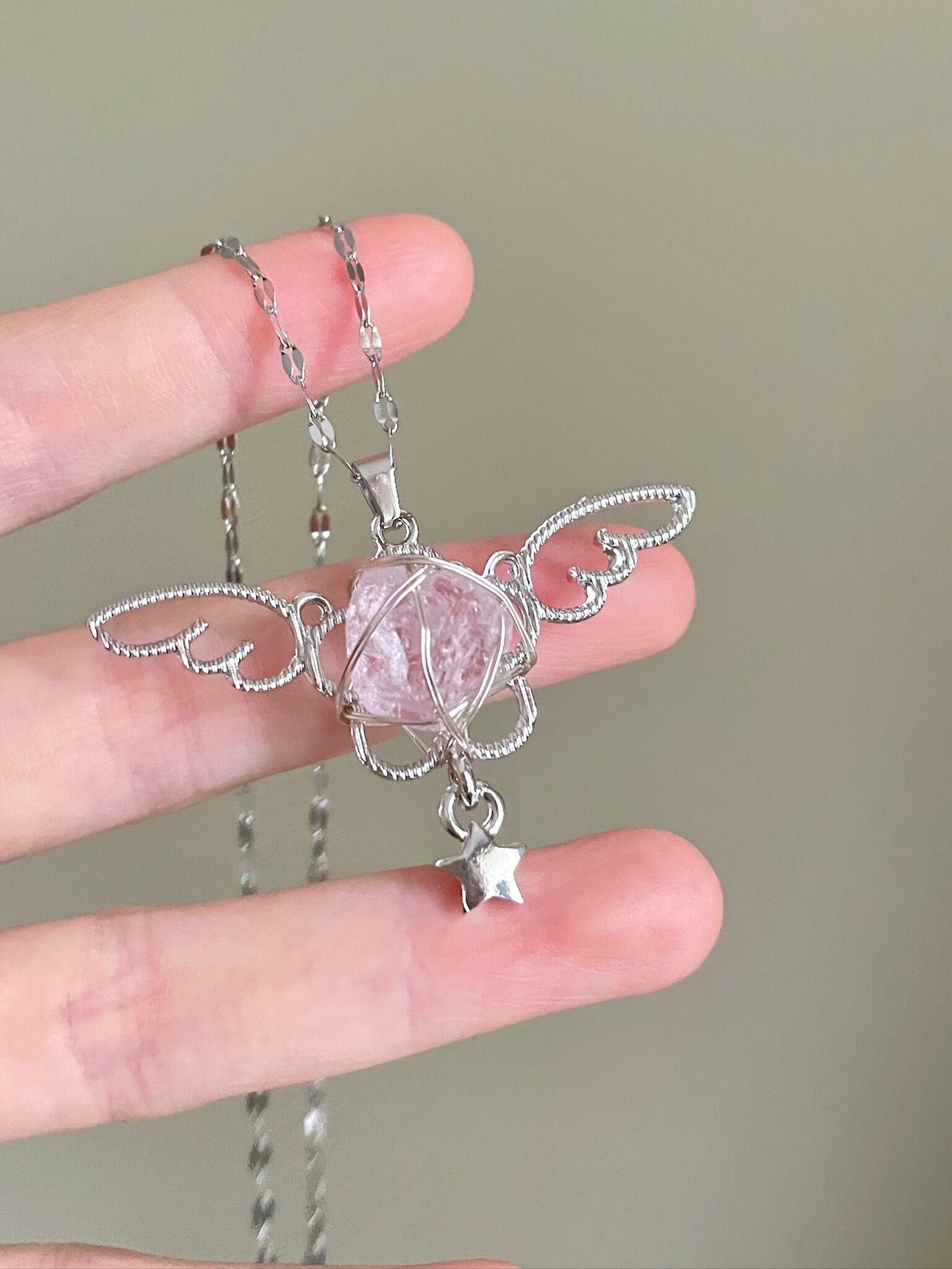 Silver angel pendant with a pink crystal held between fingers against a neutral background