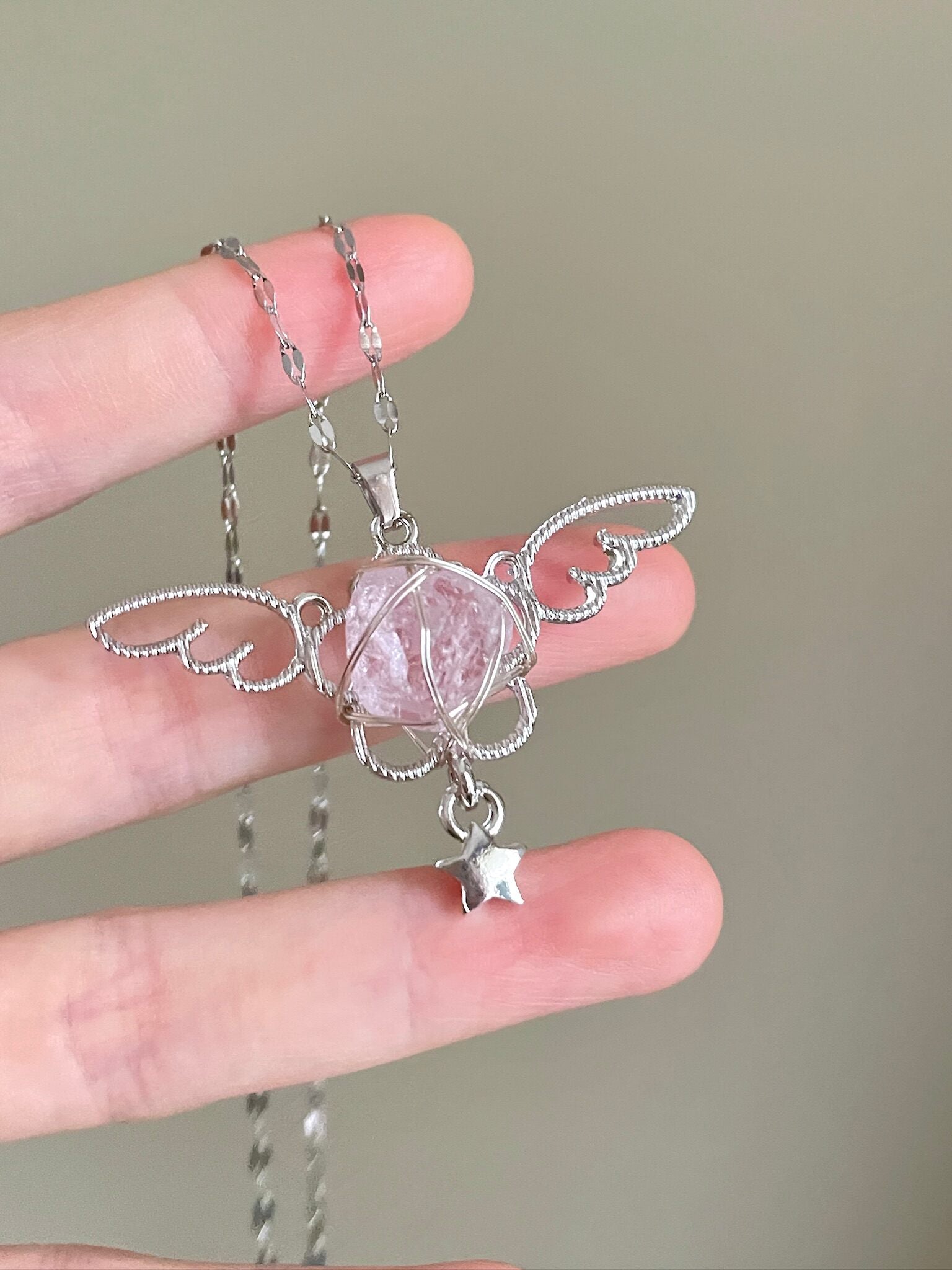 Silver angel pendant with a pink crystal held between fingers against a neutral background