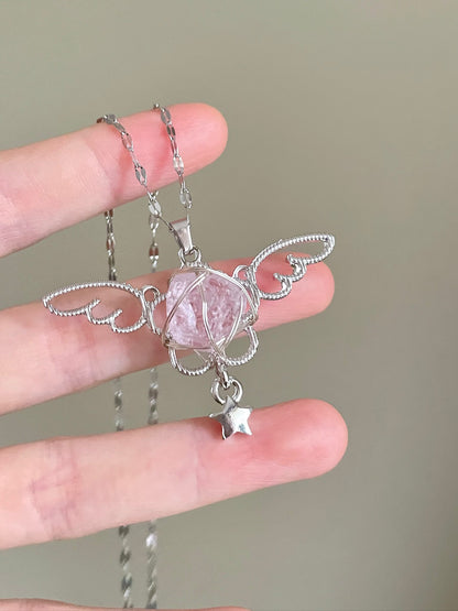 Silver angel pendant with a pink crystal held between fingers against a neutral background