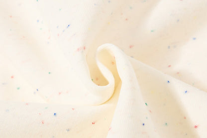 A close-up of cream-colored fabric with tiny scattered multicolor flecks, shown with a soft fold in the center.