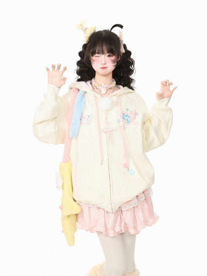 A model wearing a pastel-colored Lolita-style outfit, featuring a cream-colored zip-up hoodie with pink and blue accents, a pink ruffled skirt, and a yellow plush accessory, posed against a solid white background.
