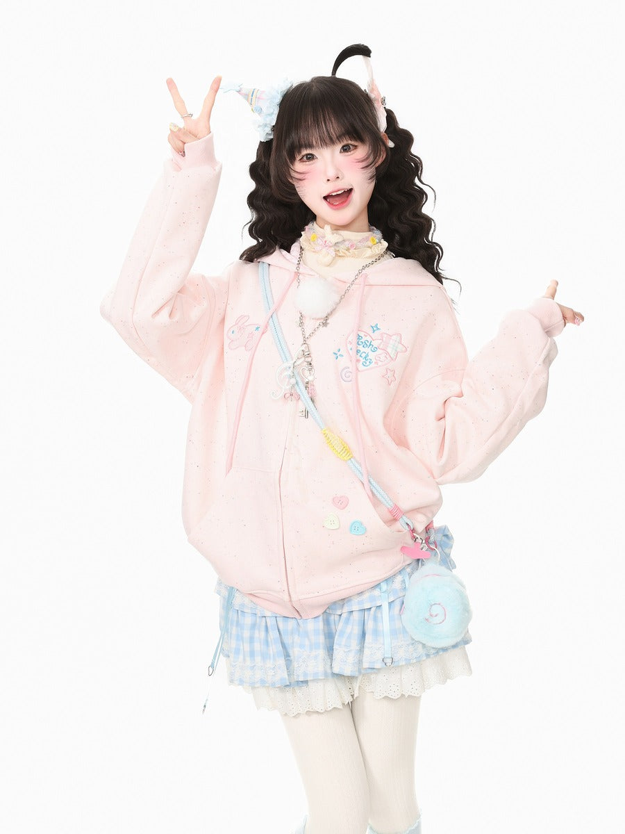 A young woman posing in a pastel pink zip-up hoodie with cute cartoon graphics, a blue and white gingham pleated skirt, and a small light blue crossbody bag, set against a solid white background.
