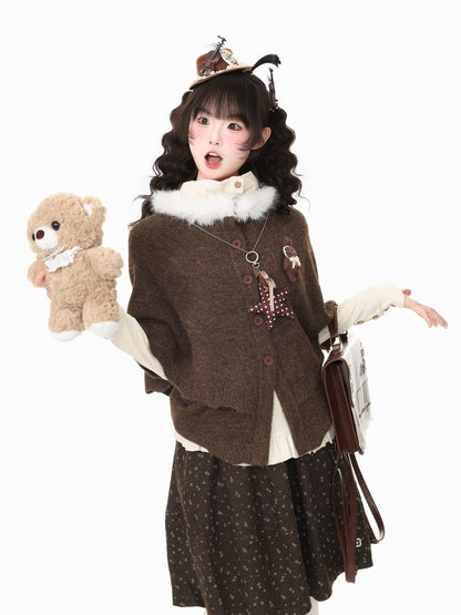 A young woman modeling a brown knit cardigan with a white faux-fur collar, styled with a dark patterned skirt, cream sleeves, a brown teddy bear plush, and a small hat against a plain white background.